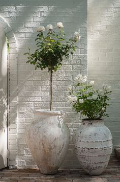 two white vases sitting next to each other on top of a brick floor near a wall