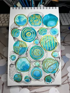 a drawing with blue and yellow circles on paper next to a computer keyboard, pencils and markers