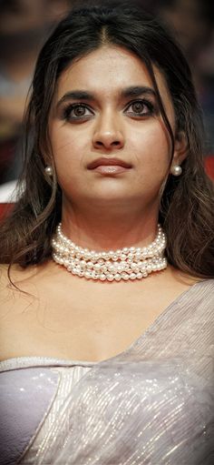 a woman in a silver dress with pearls on her neck and shoulder, looking at the camera