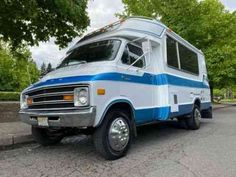 a white and blue bus is parked on the side of the road in front of some trees