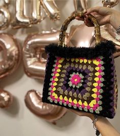 a hand holding a crocheted purse in front of some foil balloons and other decorations