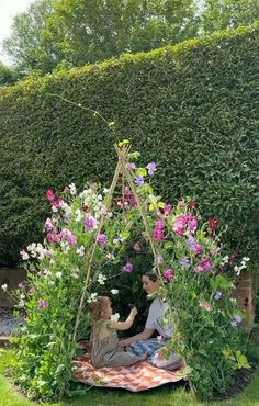 two people sitting on a blanket in the middle of a garden with flowers around them