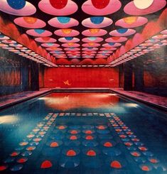 an indoor swimming pool surrounded by red and blue circles on the ceiling, with lights above it