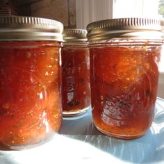 three jars filled with food sitting on top of a white table covered in sun light