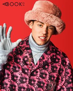 a man wearing a pink hat and coat with his hands in the air while standing against a red background