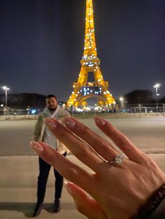 a person's hand with their engagement ring in front of the eiffel tower