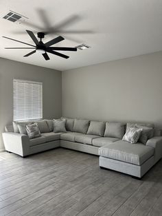 a living room with a large sectional couch and ceiling fan