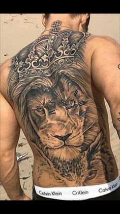 a man with a lion and crown tattoo on his back is standing in front of the ocean