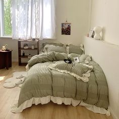 an unmade bed sitting next to a window in a room with wooden floors and white curtains