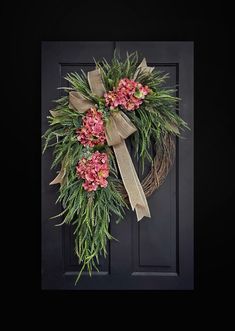 a wreath with pink flowers and greenery hangs on a door frame in front of a black background