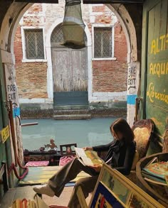 a woman sitting in a chair reading a book next to an open doorway with a bell hanging from the ceiling