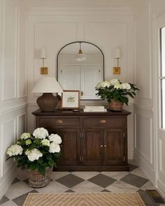 there is a vase with white flowers on the dresser in this entryway, along with two lamps and a mirror