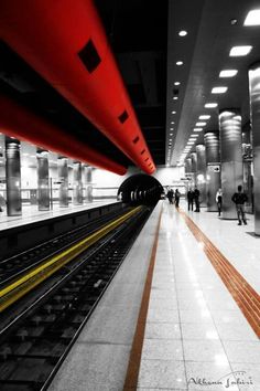 a train station with people standing on the platform and one person walking down the track