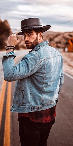 a man wearing a hat and jacket standing in the middle of an empty road with his hand on his hip