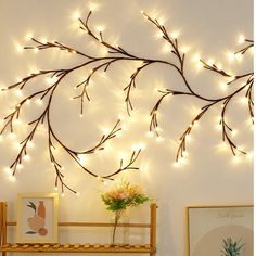 there is a wall decoration with lights on the branches and flowers in front of it