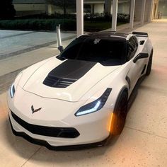 a white sports car parked in front of a building with its hood up and lights on