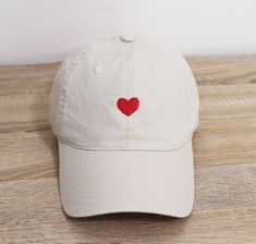 a white baseball cap with a red heart embroidered on the front and back side, sitting on a wooden surface