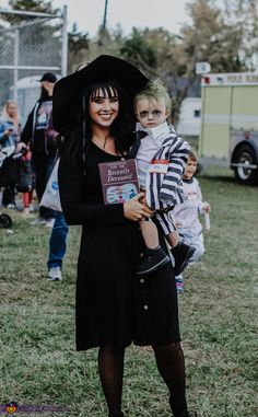 a woman holding a child in her arms while standing on top of a grass covered field