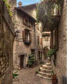 an alley way with stone buildings and steps leading up to the second floor, surrounded by greenery