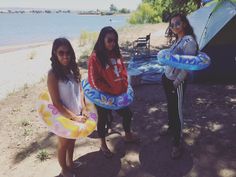 three girls are holding inflatable floats on the beach near a tent and water