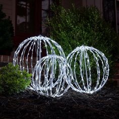 two white wire ball lights sitting on the ground in front of a house at night