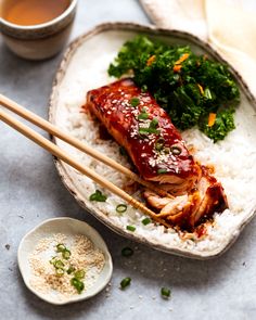 meat and vegetables on rice in a bowl with chopsticks next to the plate