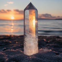 a crystal point sitting on top of a sandy beach next to the ocean at sunset