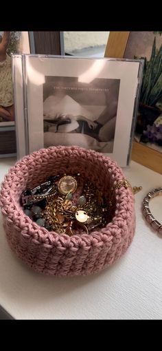 a pink knitted basket sitting on top of a table next to a framed photo