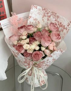 a bouquet of pink and white roses in a paper wrapper on a glass table