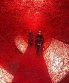 two people are standing in the middle of a large red structure that looks like yarn