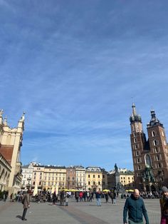 people are walking around in an old european city with tall buildings on either side and blue skies above them