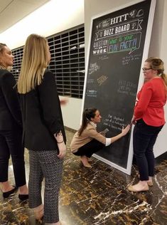 three women standing in front of a blackboard with writing on it and one woman pointing at the board