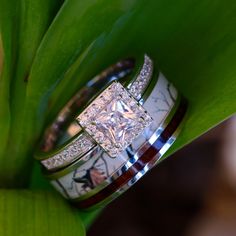 two wedding rings sitting on top of each other next to a green plant with leaves