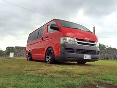 a red van parked on top of a lush green field next to a stone wall