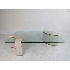 a glass and wood coffee table with an unusual shaped design on the top, in front of a white wall