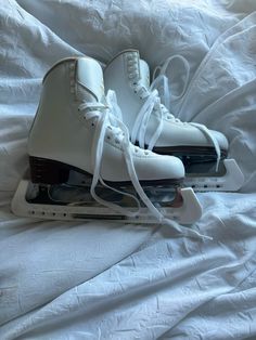 two pairs of white ice skates sitting on top of a bed