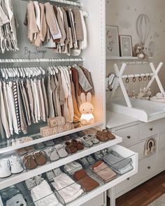 a white closet filled with lots of baby clothes and shoes on shelves next to a dresser