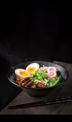 a bowl of ramen with eggs and vegetables in it on top of a wooden table