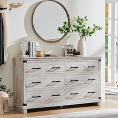 a white dresser sitting next to a window with a round mirror on top of it