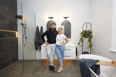 a man and woman standing next to each other in front of a bathroom with tiled walls