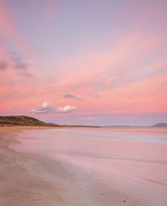 a pink sky over the ocean at sunset with waves coming in from the shore and sand on the beach