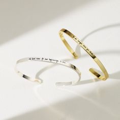 two gold cuff bracelets with words on them