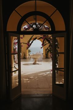 an open door leading to a courtyard with a fountain and flowers on the outside wall