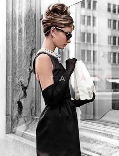 a woman in a black dress and pearls is looking at her cell phone while holding a shopping bag