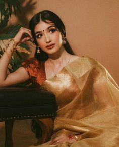 a woman sitting on top of a chair wearing a gold sari and holding her hand near her face