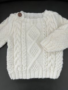 a white knitted sweater sitting on top of a black table next to a brown button