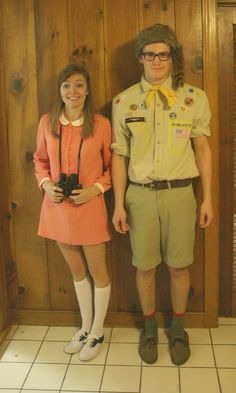 a man and woman are standing in front of a wooden paneled wall wearing costumes