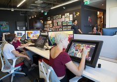 people are sitting at desks with computers and pictures on the wall in an office