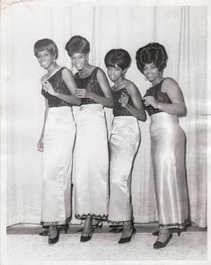 four women standing next to each other in front of a white curtain with their hands on their hipss