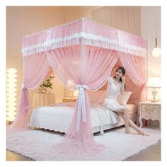 a woman sitting on top of a bed in a room with white carpet and pink curtains